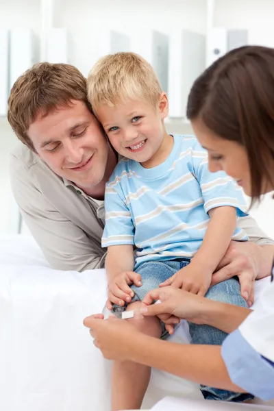 Médico aplicando um gesso no joelho de um menino sorridente — Fotografia de Stock