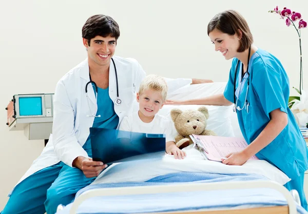 Маленький мальчик смотрит на рентген со своим врачом и медсестрой — стоковое фото