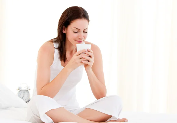 Avslappnad kvinna dricker en kaffe som sitter på sin säng — Stockfoto