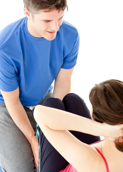 Brunette woman doing sit-ups assited by her personal trainer — Stock Photo, Image