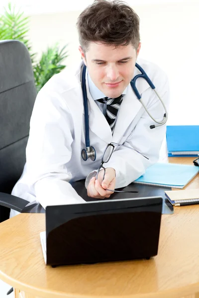 Stanowczy mężczyzna lekarz za pomocą laptopa siedząc przy biurku — Zdjęcie stockowe