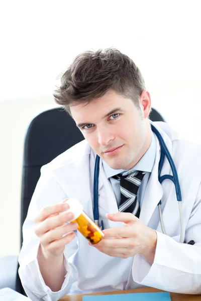 Σοβαρή αρσενικό γιατρός κρατώντας χάπια που κάθεται στο γραφείο του — Φωτογραφία Αρχείου