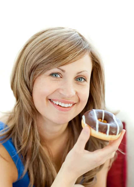 Mulher encantada está comendo um donut em um sofá — Fotografia de Stock