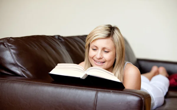 Χαμογελαστή γυναίκα διαβάζοντας ένα βιβλίο σε ένα καναπέ — Φωτογραφία Αρχείου