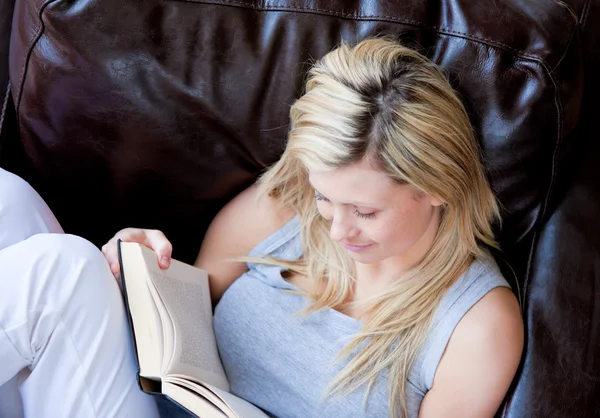 Mulher alegre lendo um livro em um sofá — Fotografia de Stock