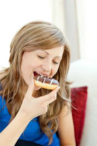Mulher radiante está comendo um donut em um sofá — Fotografia de Stock