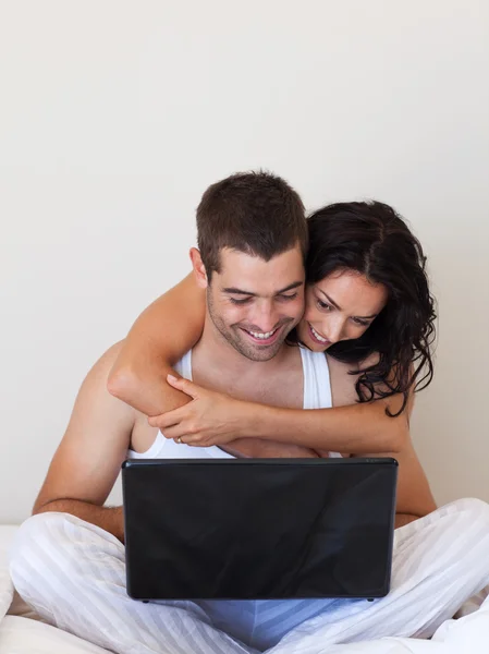 Lovely couple using a laptop sitting on a bed — Stock Photo, Image