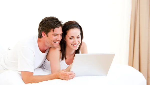 Fröhliches Paar mit einem Computer im Bett lizenzfreie Stockfotos