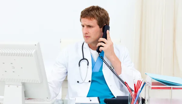 Confident doctor on phone at his computer — Stock Photo, Image