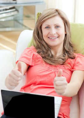 Successful woman using a laptop sitting on a sofa clipart