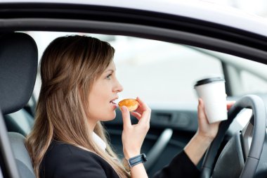 Charming businesswoman eating and holding a drinking cup while d clipart