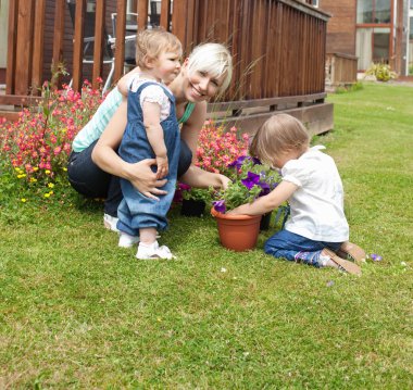 Smiling woman with two children in the garden clipart