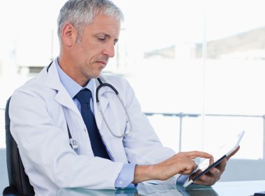 Serious doctor working with a tablet computer clipart