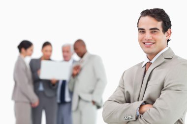 Smiling salesman with arms folded and colleagues behind him clipart