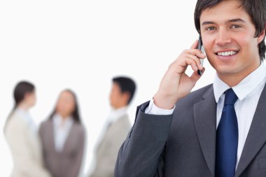 Smiling salesman on his cellphone with team behind him clipart