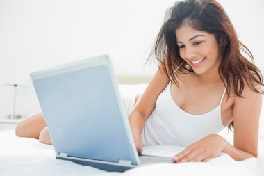 Woman lying across her bed, using her laptop and enjoying what s clipart