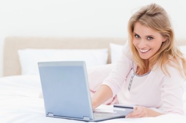 Woman lying on the bed, with a laptop in hand and looking forwar clipart