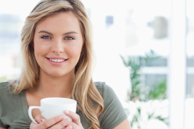 Woman holding a mug in her hands and smiling, while looking forw clipart