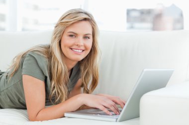 Woman lying across the couch with laptop in front of her, smilin clipart