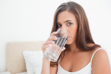 Woman looking forward drinking from a glass of water clipart