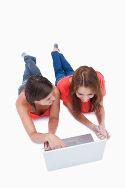 Teenage girl using a laptop while looking at her friend and lyin clipart