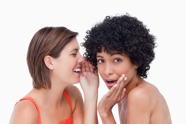 Teenage girl whispering a secret to a surprised friend clipart