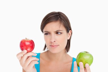 Teenage holding two apples and looking at the red one clipart