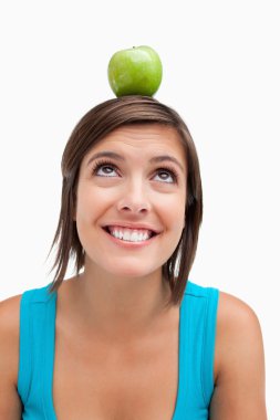 Smiling teenage girl trying to look at a green apple placed on h clipart