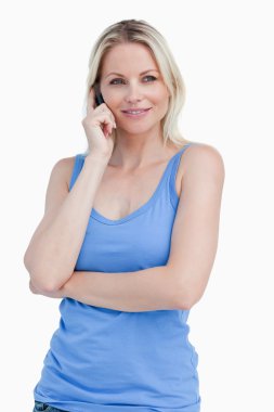 Blonde woman using a cellphone while standing with herarms cross clipart