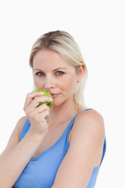 Blonde woman holding a green apple close to her mouth clipart