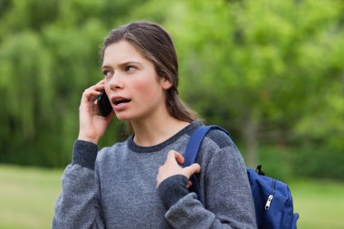 Young calm girl talking on the phone while looking towards the s clipart