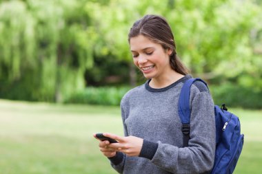 Smiling teenage girl using her cellphone while receiving a text clipart