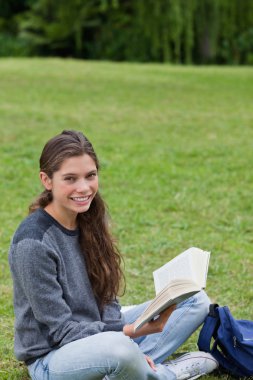 Young smiling girl sitting cross-legged while holding a book clipart