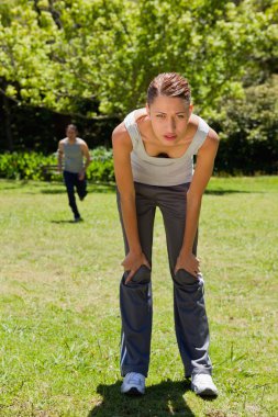 Woman bending over while a man is running in the background clipart