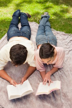 Elevated view of two friends reading while on a lying down clipart