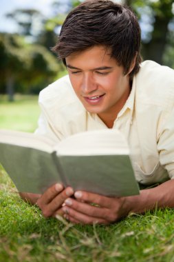 Man smiling while reading a book as he lies down clipart