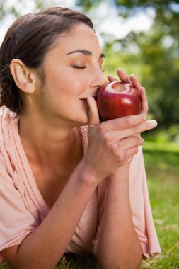 Woman smells an apple while lying in grass clipart