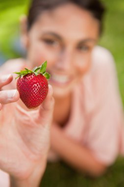 Woman holding a strawberry at arms reach clipart