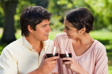 Two friends looking at each other while touching glasses of wine clipart