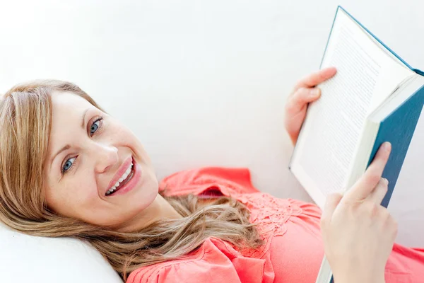 Cheerful woman reading a book lying on a sofa — Stock Photo, Image