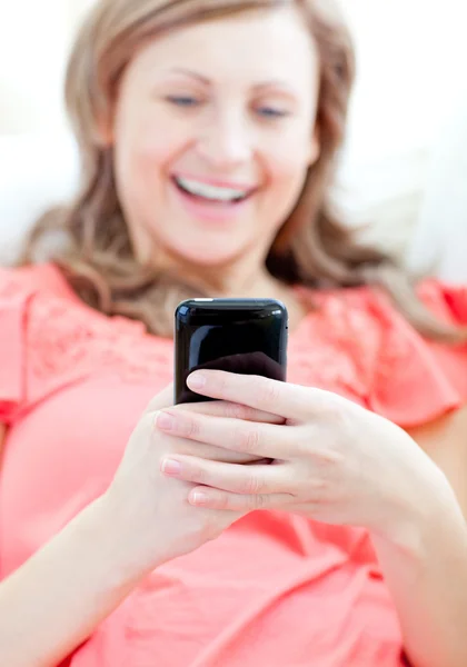 Laughing woman sending a text lying on a sofa — Stock Photo, Image