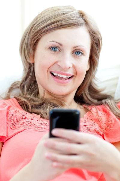 Strålande kvinna skicka en text liggande på en soffa — Stockfoto