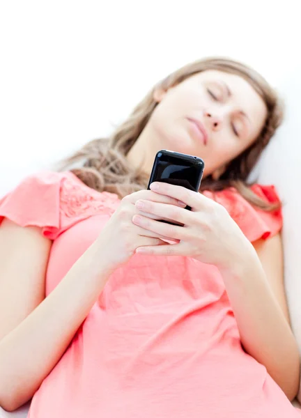 Mujer cansada enviando un mensaje de texto tumbado en un sofá —  Fotos de Stock