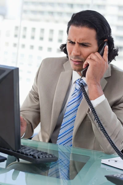Porträtt av en förvirrad affärsman som arbetar med en bildskärm samtidigt som den är på telefonen — Stockfoto