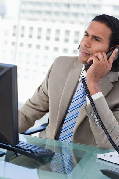 Retrato de um empresário confuso que trabalha com um monitor enquanto está ao telefone — Fotografia de Stock