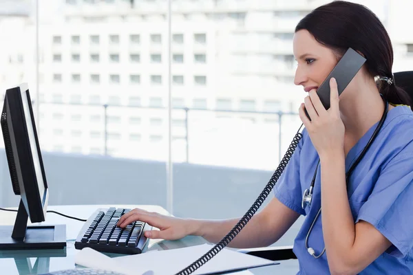 Female doctor on the phone while using a monitor — Stock Photo, Image