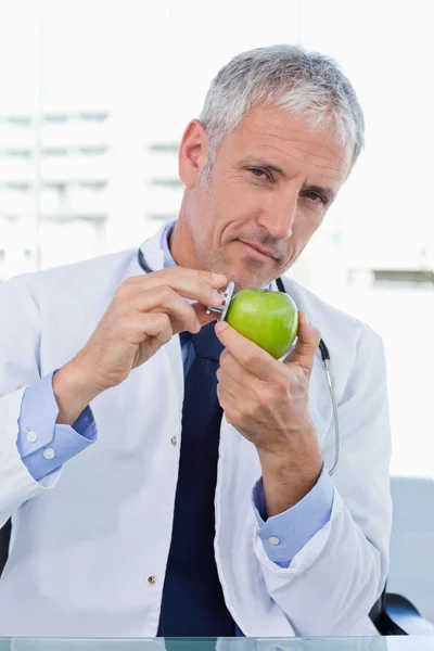Retrato de um médico colocando seu estetoscópio em uma maçã — Fotografia de Stock