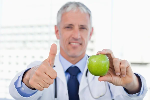 Портрет доктора, показывающего яблоко с большим пальцем вверх — стоковое фото