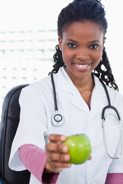 Portræt af en smilende kvindelig læge, der viser et æble - Stock-foto