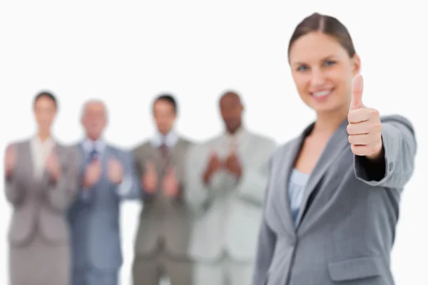 Lächelnde Geschäftsfrau mit erhobenem Daumen und Kollegen hinter sich — Stockfoto